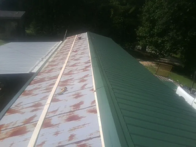 Old rusted panels beside newly installed green metal roofing — Wind Damage Roof Repair by Roofing Brothers in Inwood