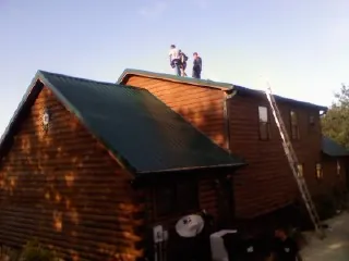 Crew on the ridge of a green metal roof on a two story log home in Inwood