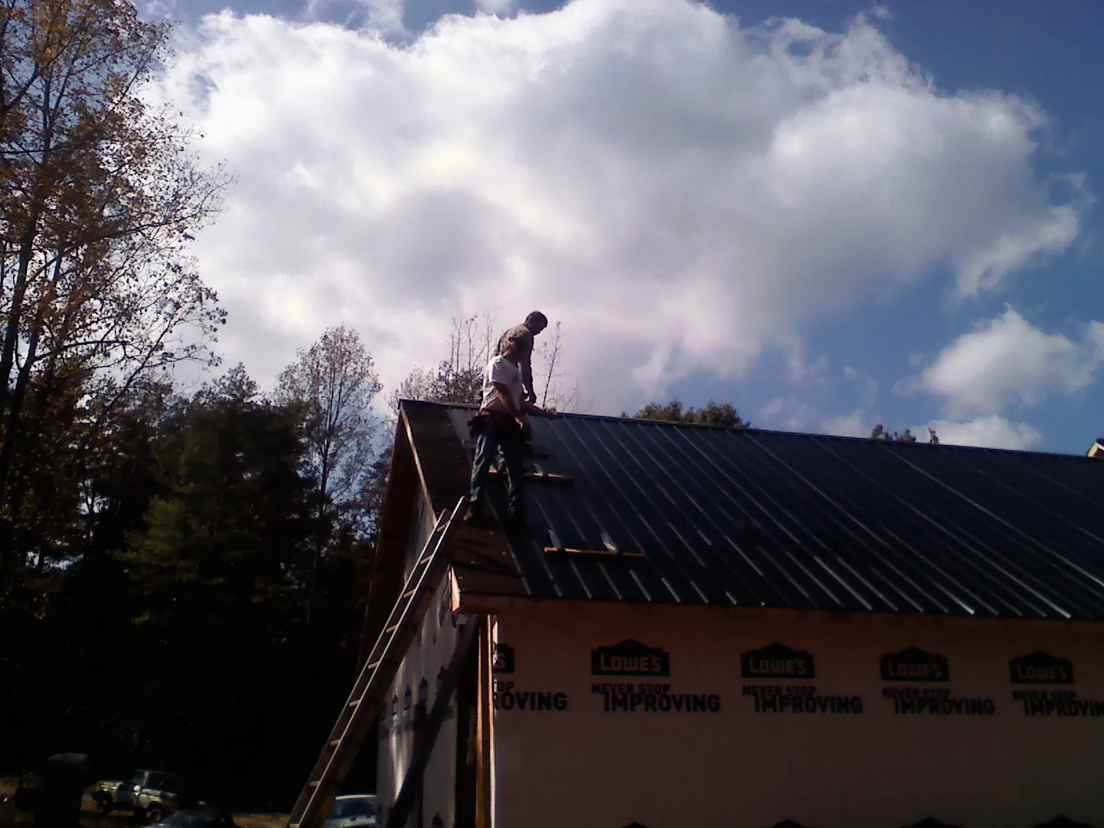 Roofer fastening dark metal panels high against a cloudy sky, from a Roof Inspection job in Inwood