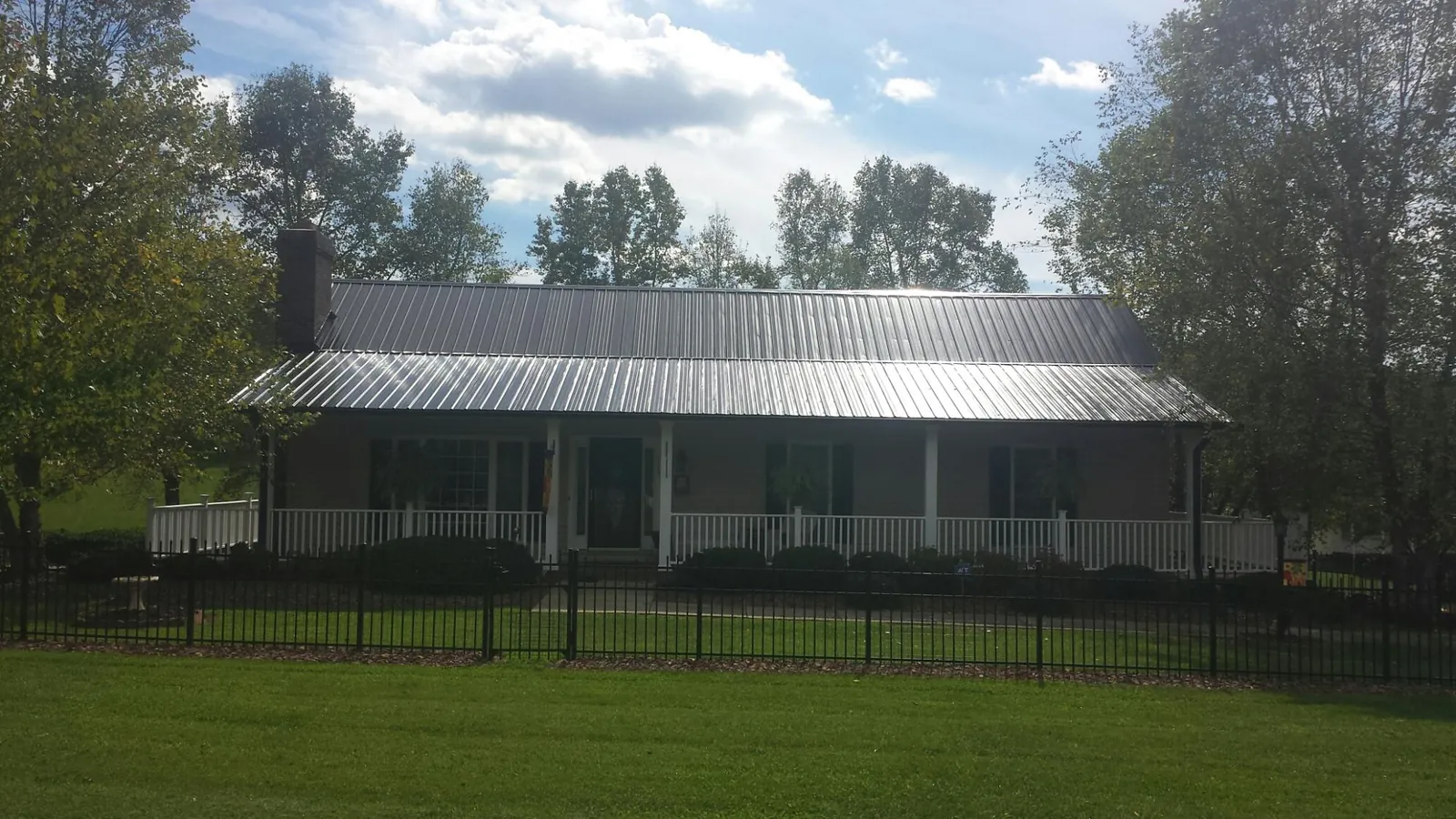 Gray metal roof on a brick ranch with a full width front porch — Gutter Guard Installation work by our crew in Inwood