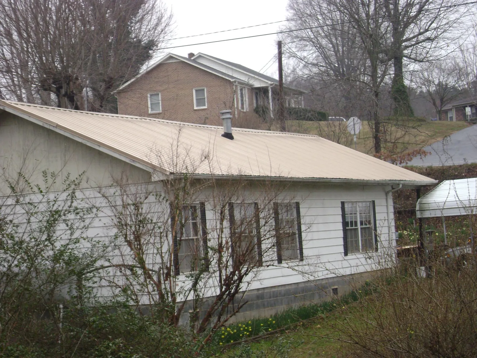Tan metal roof on a white sided house set into a hillside — Commercial Roofing by Roofing Brothers in Inwood